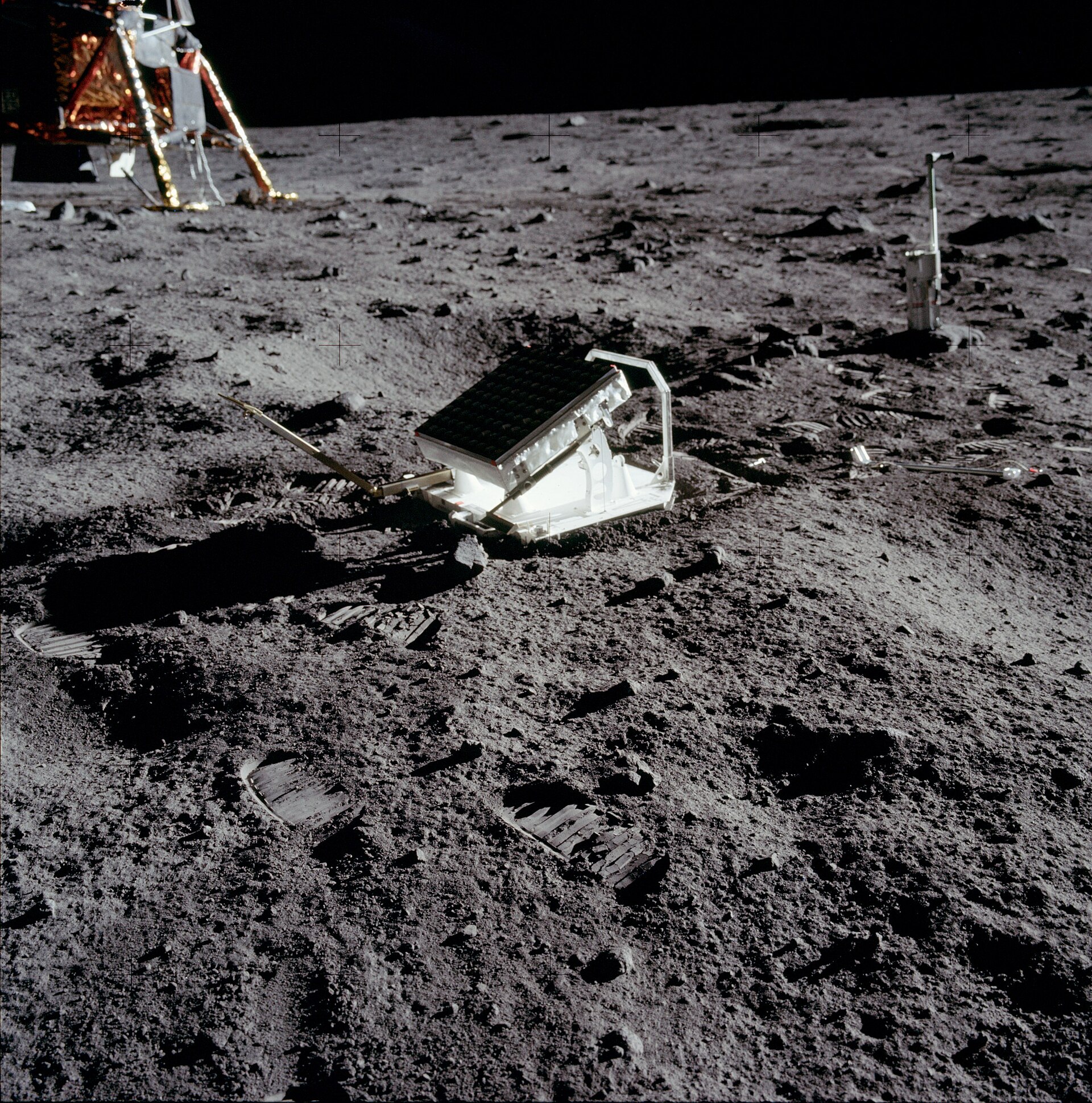 Foto de um retrorefletor (uma caixa branca com o topo reflexivo) em solo lunar, tirada na altura de uma pessoa. Ao fundo, o espaço escuro.