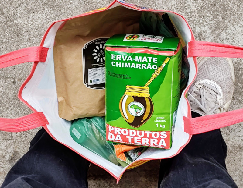 Foto de cima de uma sacola de compras, aberta, contendo café e erva mate.