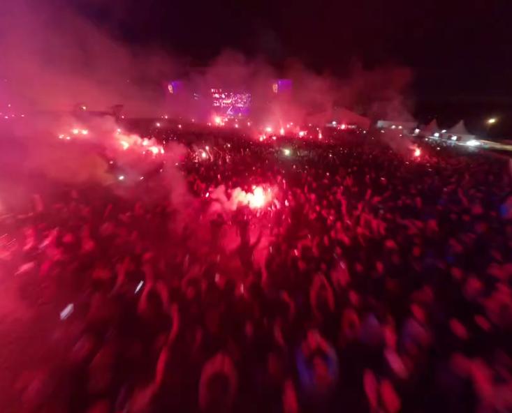 Foto area do público no estádio com vários focos de sinalizadores.